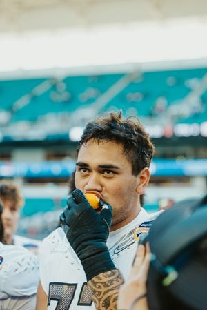 Football player in white uniform taking a bite of an orange on the sidelines.