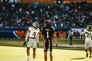 Players in white uniforms line up on a football field during a sunny game day.