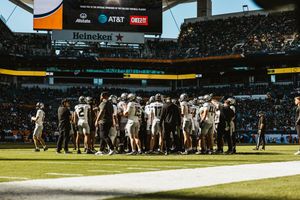 Wide panoramic view of a football stadium with teams gathered on the field during a game.