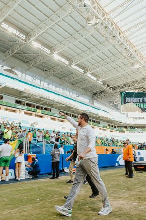 People performing synchronized dance moves in an indoor sports facility with white ceiling and artificial turf floor.