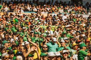 Large crowd of fans wearing green jerseys cheering enthusiastically at a sports stadium.