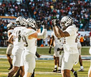 Football players celebrate on the field wearing white uniforms during a game.