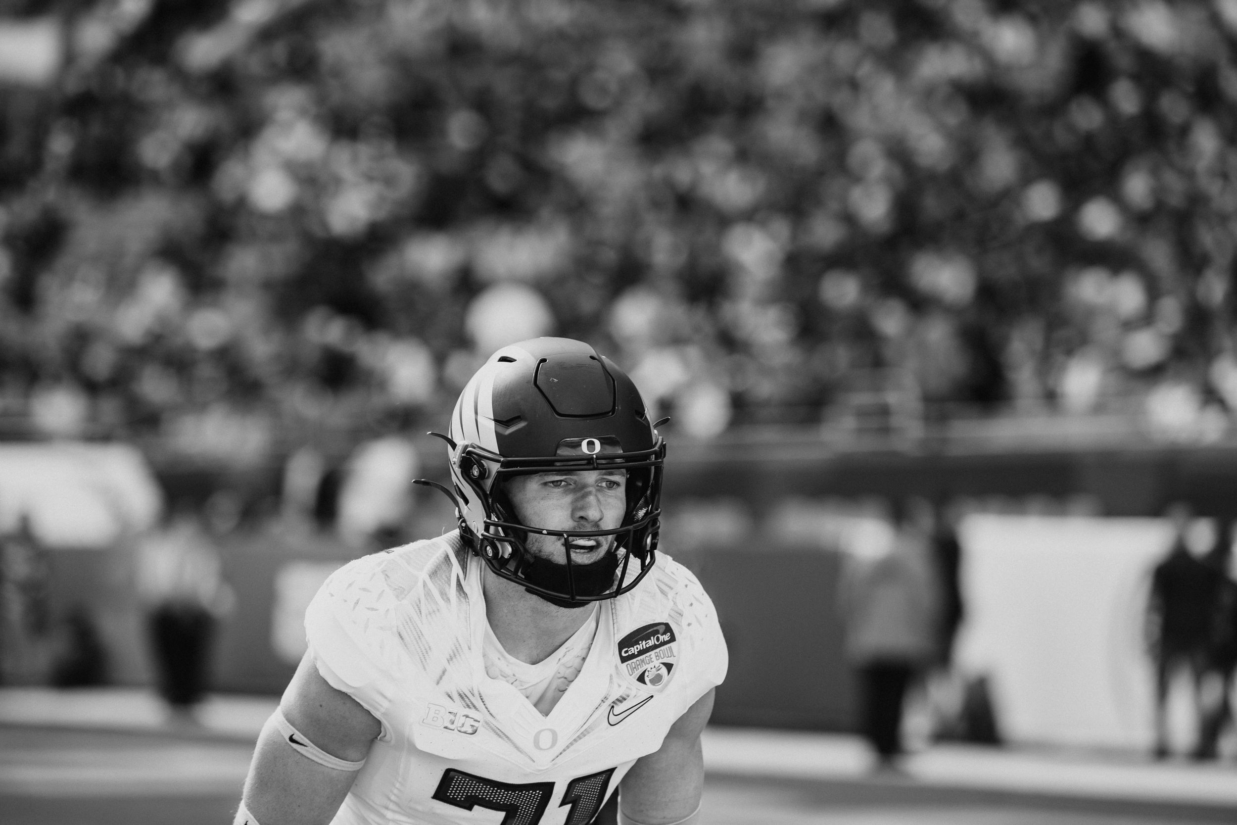 Black and white photo of a football player wearing a helmet and jersey on the field during a game.