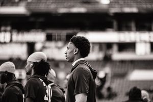 Football players and staff gather on the field in black and white monochrome photography.