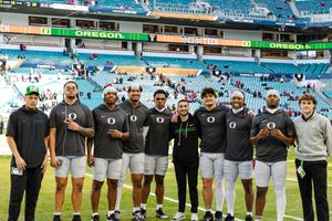 Football team members line up on the field wearing white and dark uniforms for a group photo.