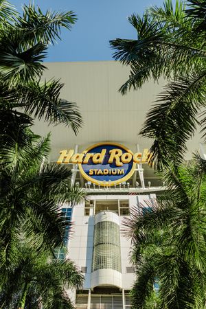 Hard Rock Stadium exterior with palm trees and signage against a bright blue sky.