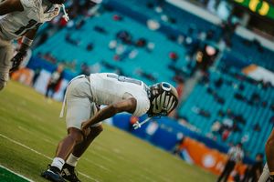 Football players in white uniforms compete for possession during an intense match at a stadium with teal seats.