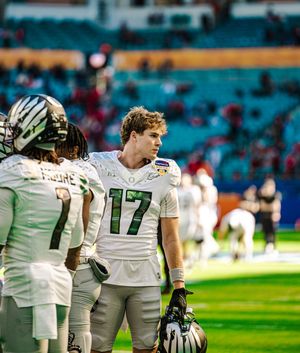 Football players in white uniforms with green numbers stand on the field during a game.