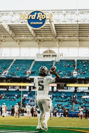 Football player in white uniform catching a pass at Hard Rock Stadium with teal seats in background.