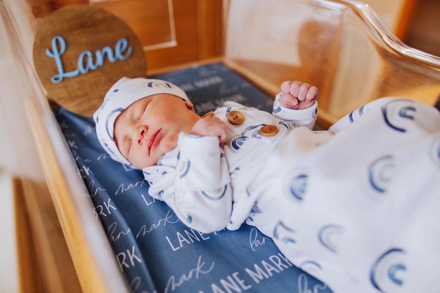 Newborn baby named Lane sleeping in a bassinet wrapped in a personalized white and navy printed blanket.