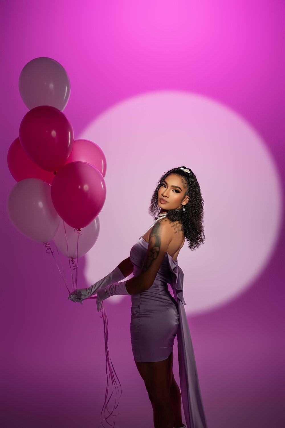 Artistic fashion photography with balloons and dramatic spotlight on purple background.