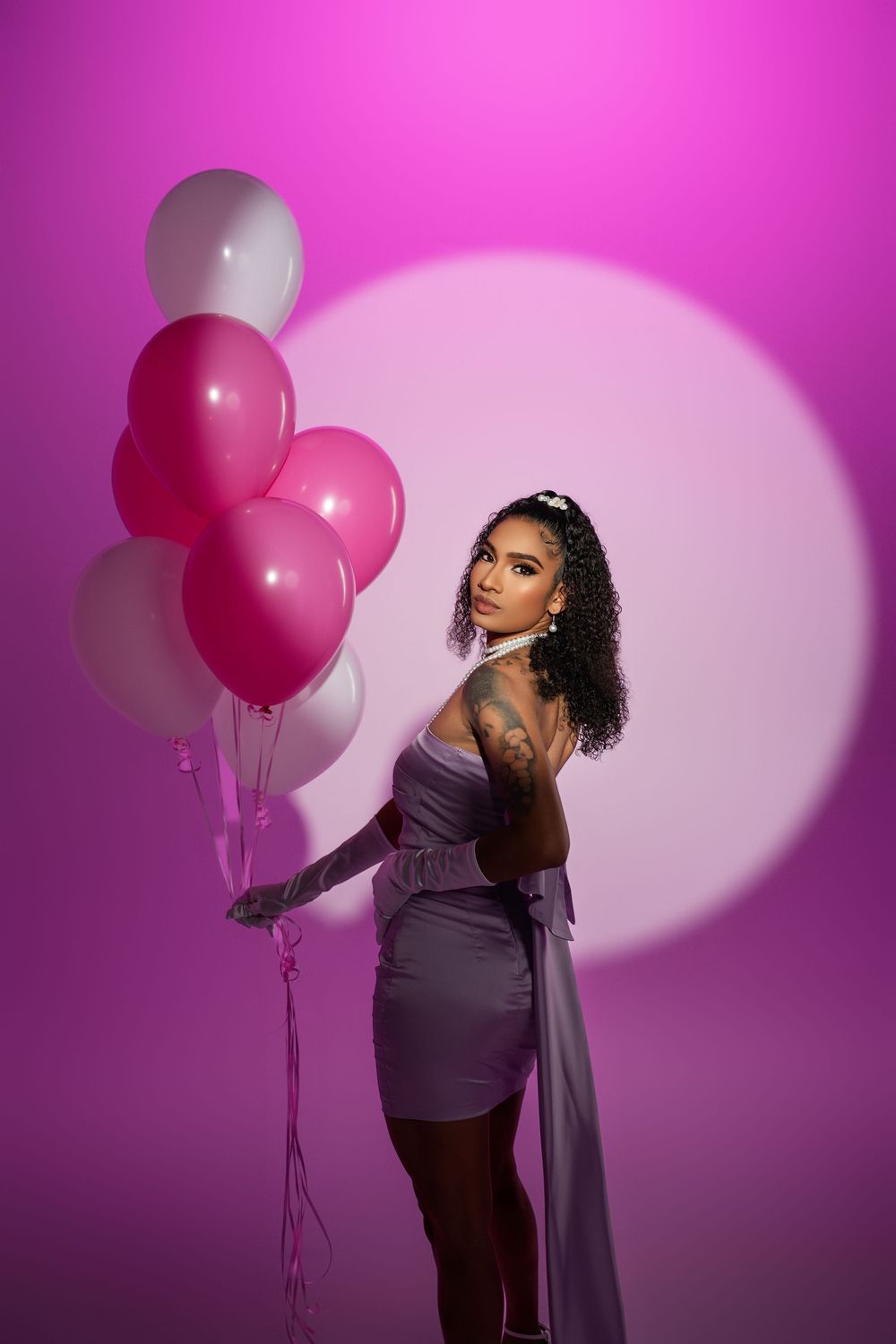 Artistic portrait session featuring purple dress and balloon props with magenta lighting.