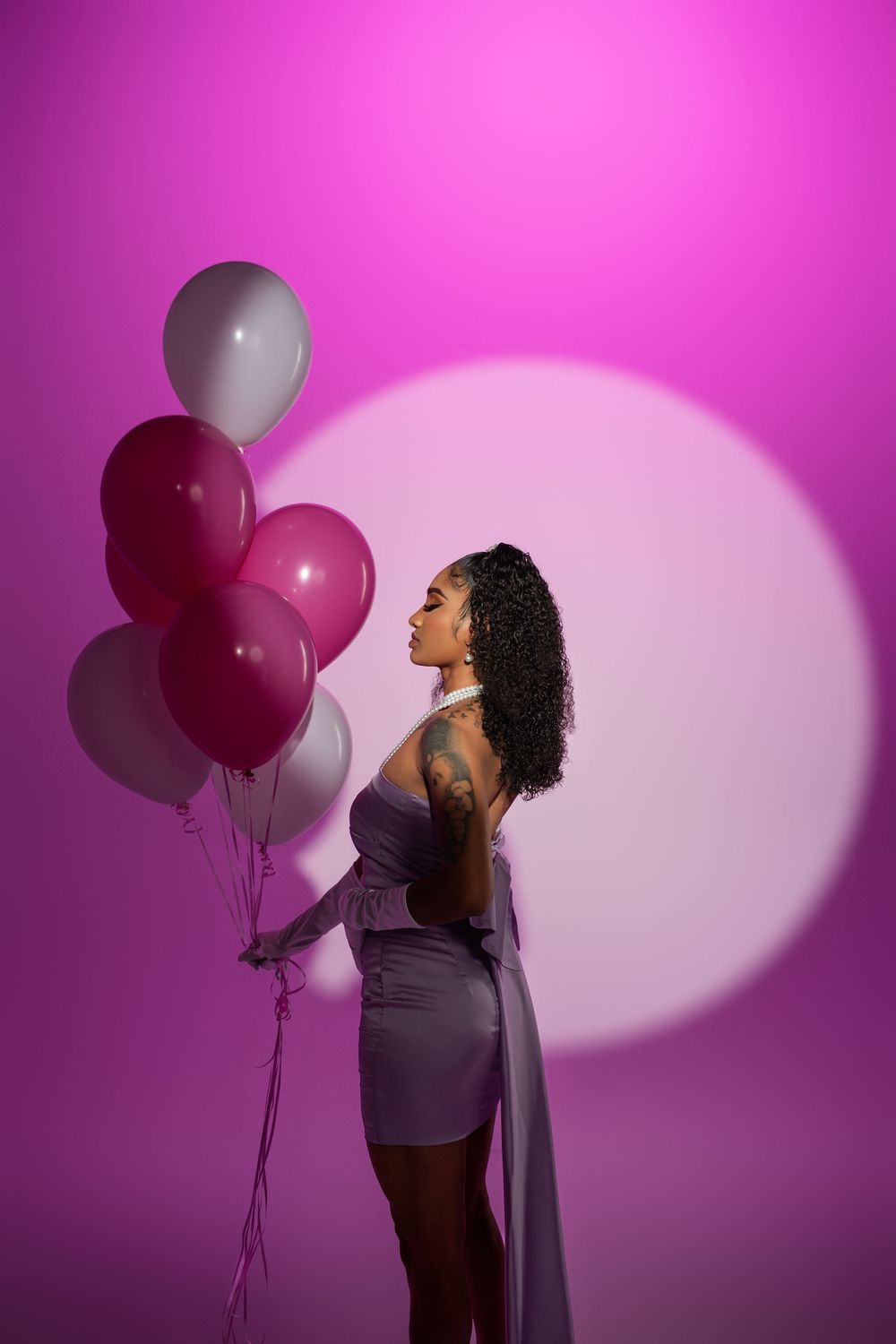 Fashion model poses with pink and white balloons against vibrant magenta backdrop in dramatic lighting.