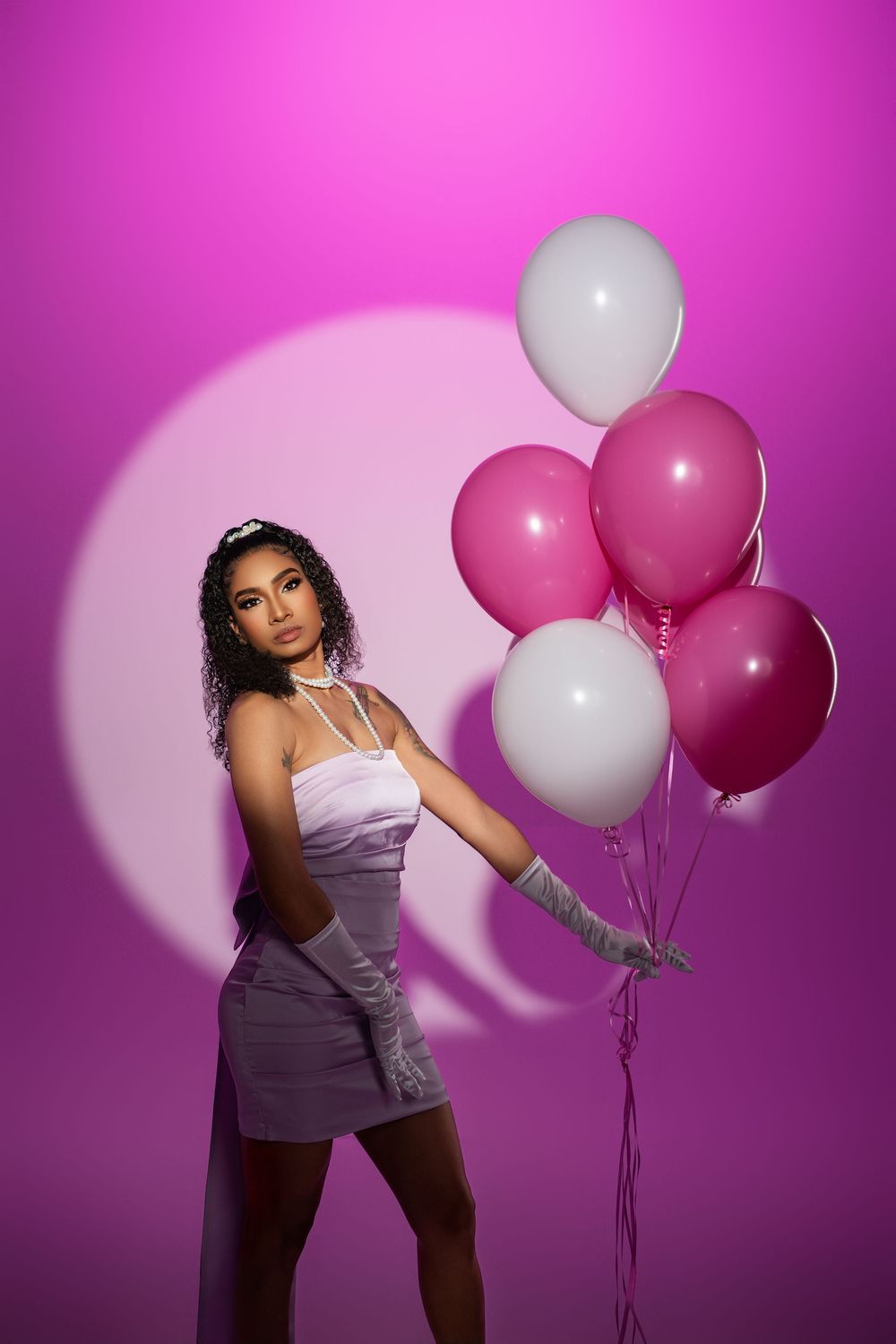 Fashion photoshoot with pink and white balloons against vibrant magenta backdrop featuring glamorous poses.