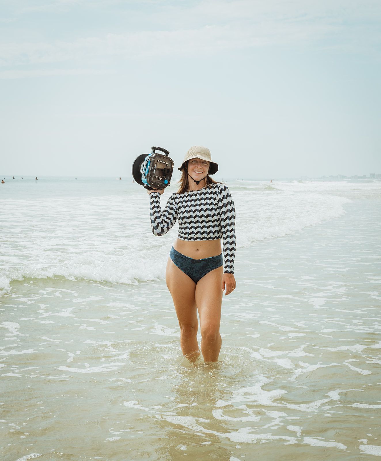 A person wearing a striped top and shorts wades in shallow ocean water on a bright sunny day.
