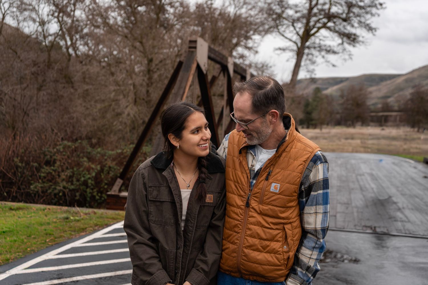 A couple in winter attire embraces on a winding mountain road on an overcast day.