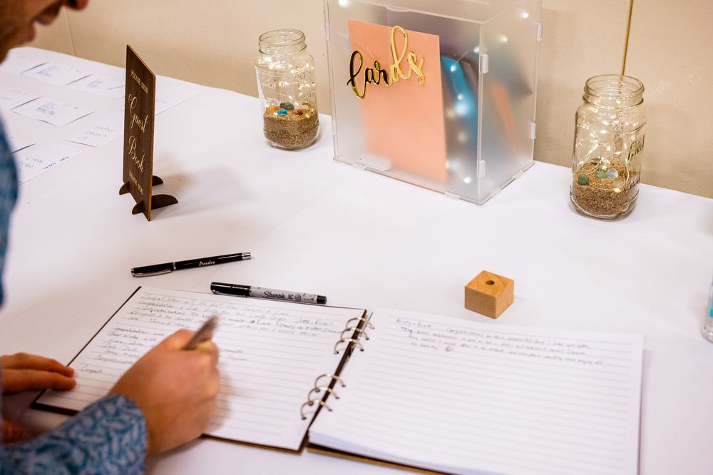 Multiple hands writing in notebooks and journals on a white table with mason jars visible.