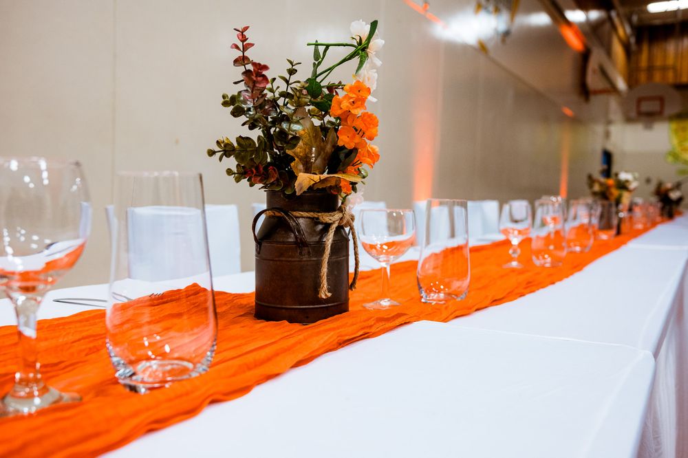 Orange table runner with wine glasses and floral centerpieces set up for an elegant event.