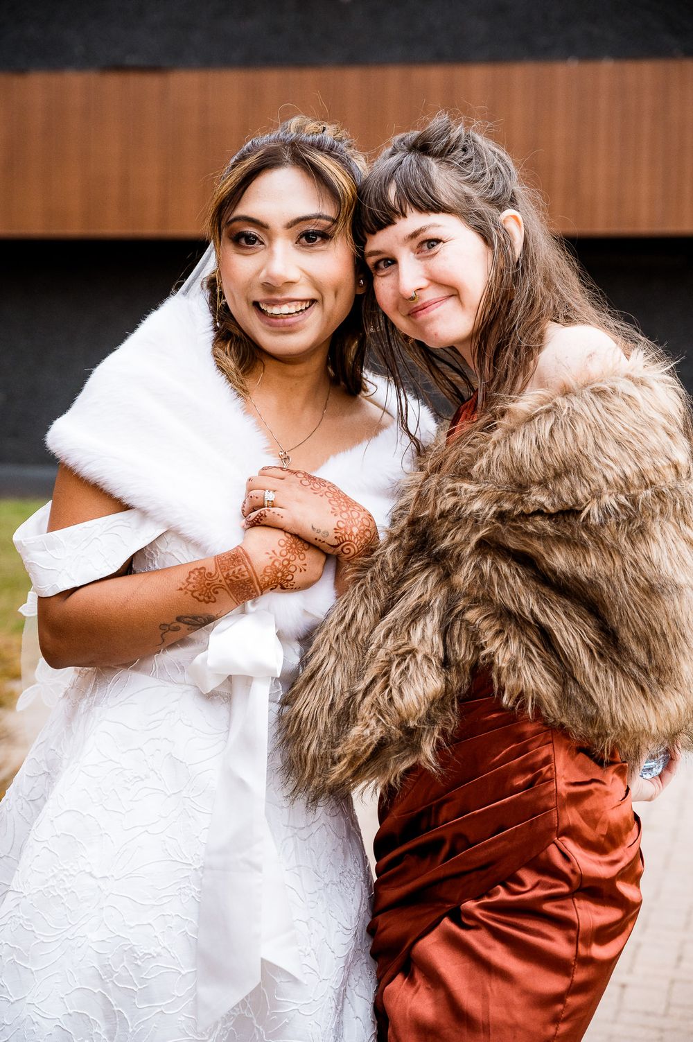 Two friends share a warm embrace while wearing contrasting white and rust-colored outfits in a candid photo series.