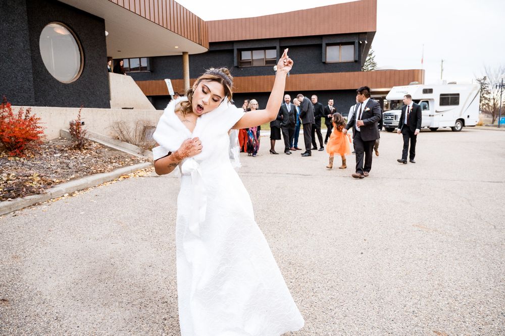 Wedding party poses outdoors near a building entrance with flowing white dresses and formal attire.