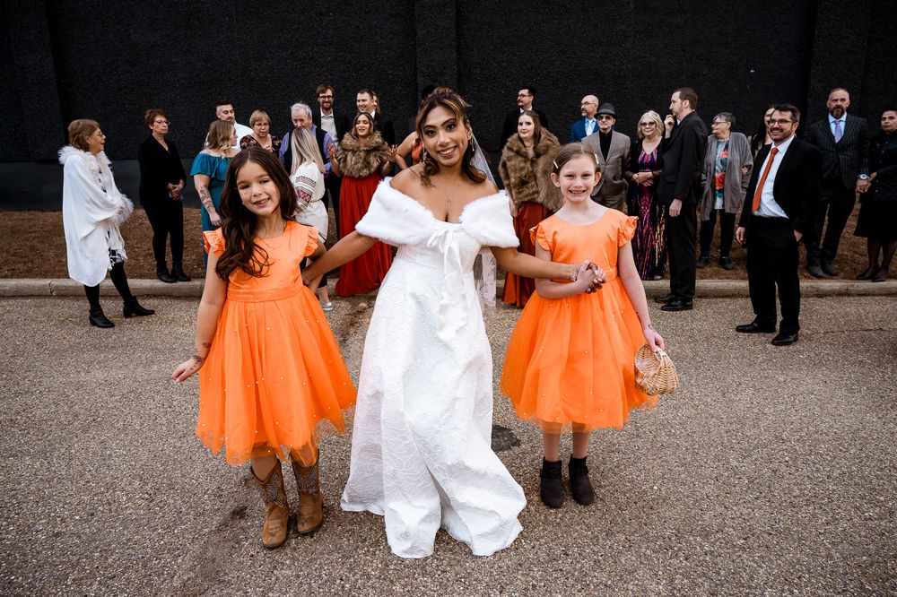 A wedding party poses outdoors with bridesmaids in vibrant orange dresses contrasting with white attire.