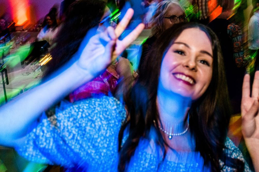 Person in blue top dancing at a nightclub with colorful lights and motion blur effects in the background.