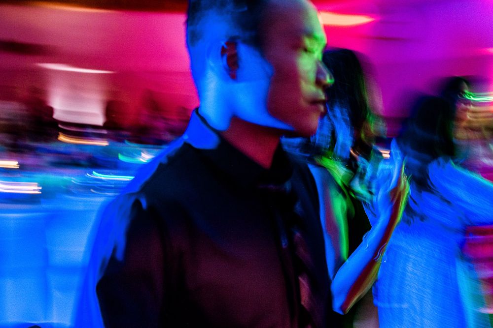 A blurred motion sequence of people dancing in a nightclub with vibrant blue and purple lighting effects.