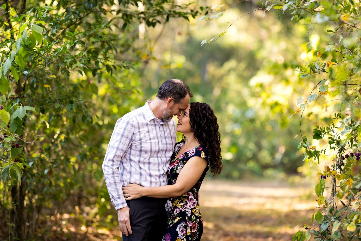 A romantic moment captured between a couple in a sunlit garden path surrounded by lush greenery.