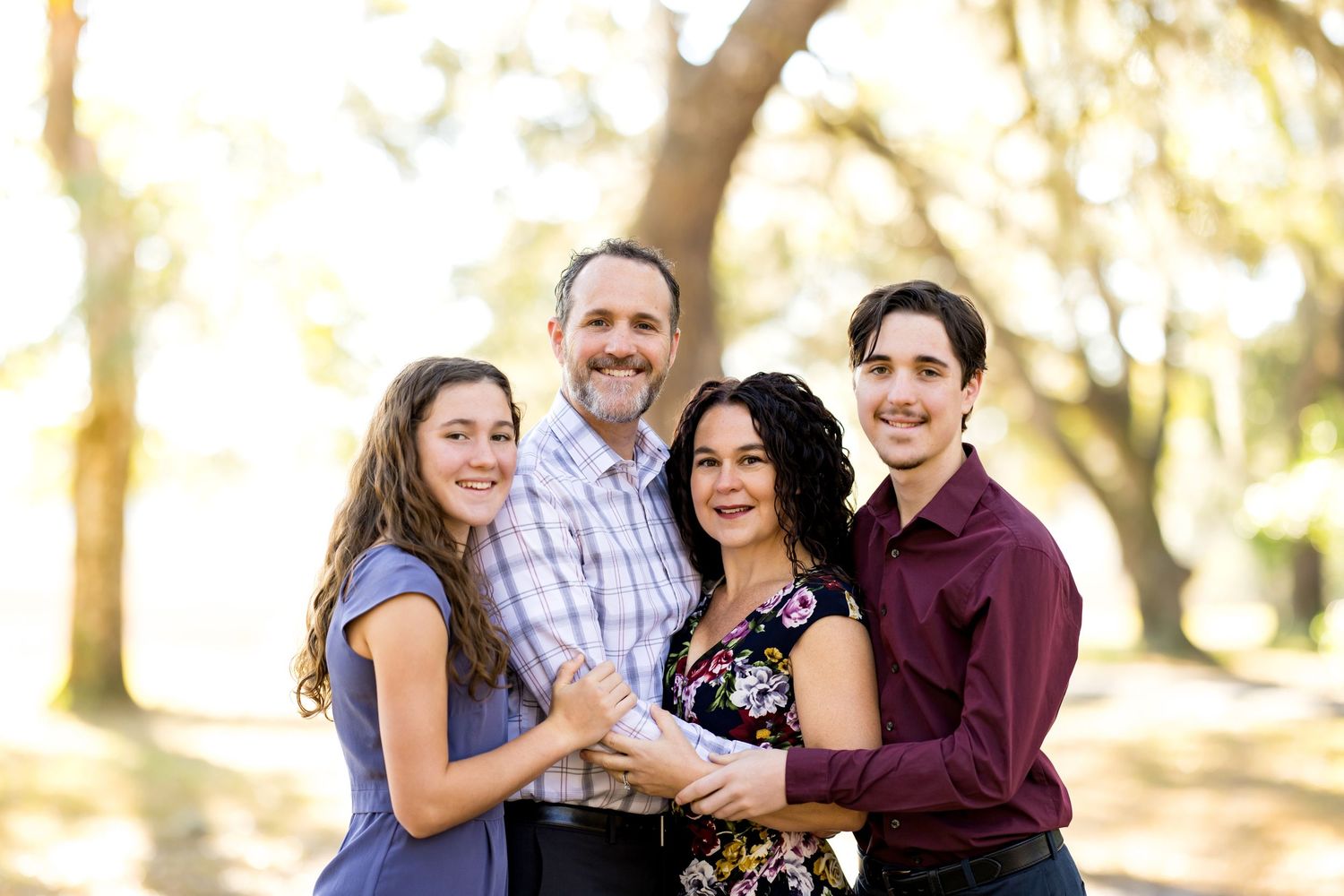 A family group poses together outdoors in a wooded setting during golden hour lighting.