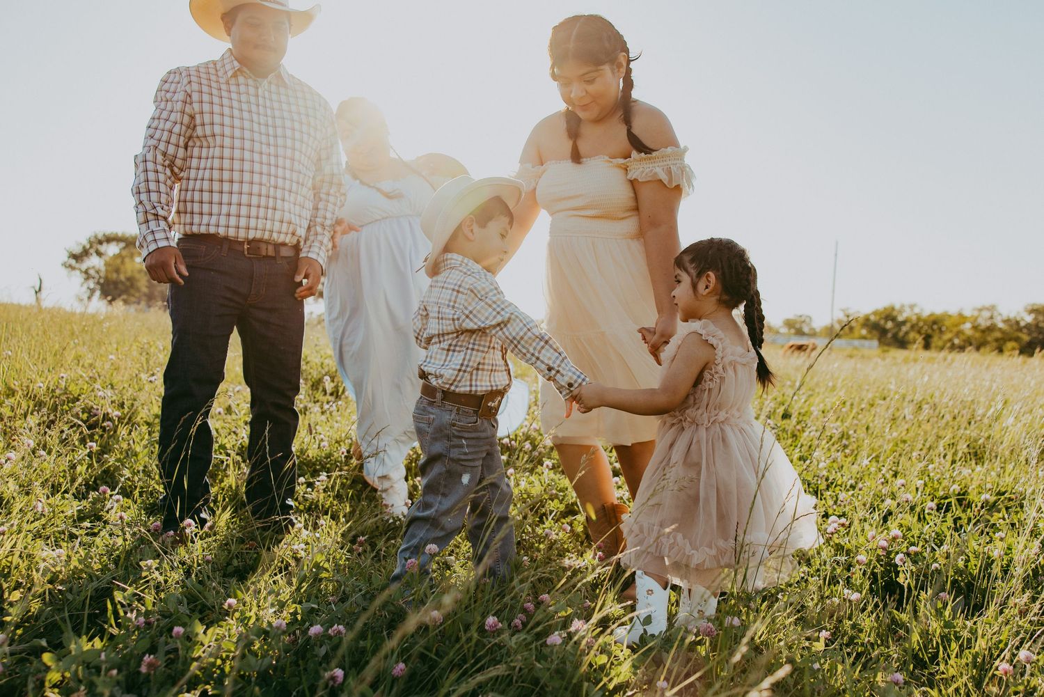 Family of four enjoying a sunny day in a green meadow, with children playing and parents watching in warm golden light.