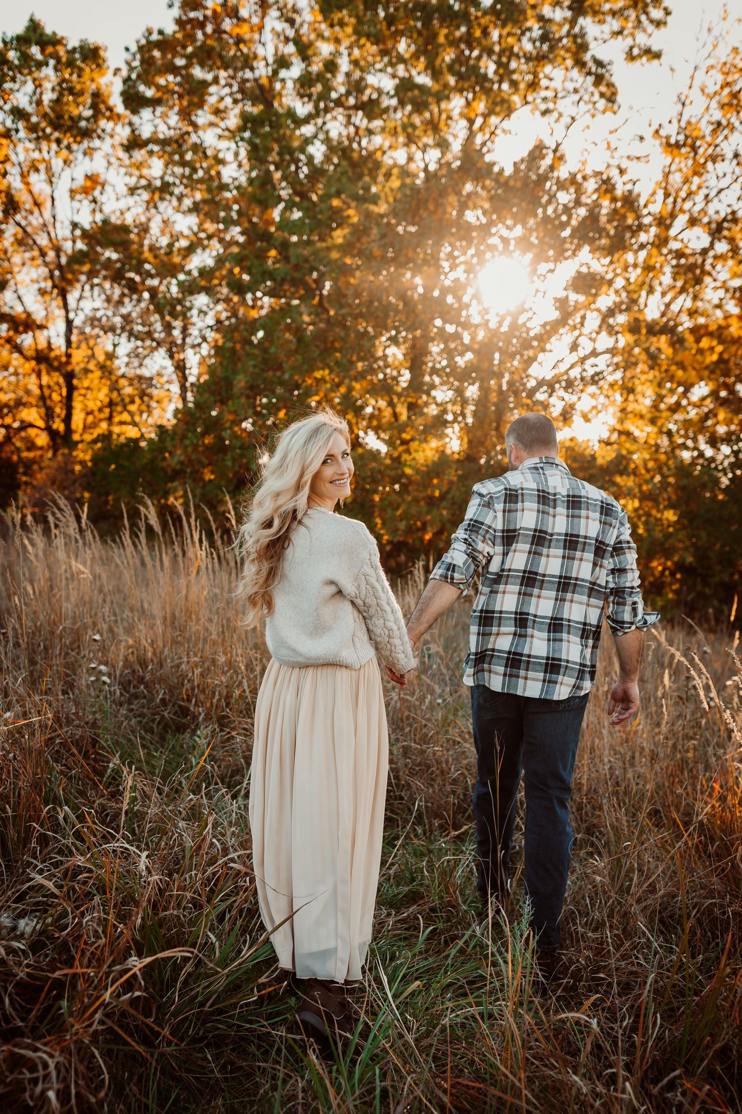 Couple walking through tall grass during golden sunset in an autumn field.