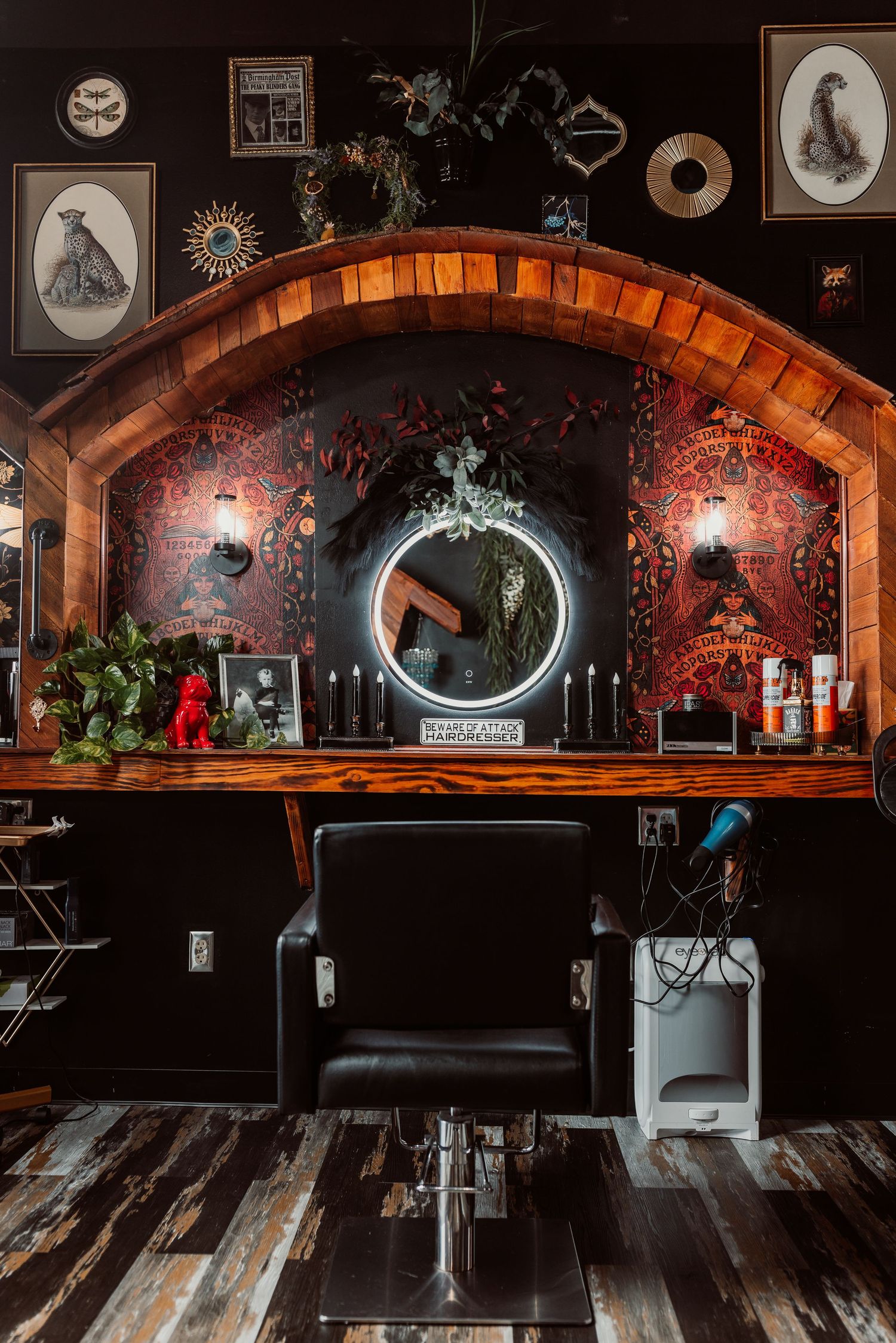 Gothic-themed barber shop with black leather chair, arched wood frame, round lit mirror, and dark ornate decor.