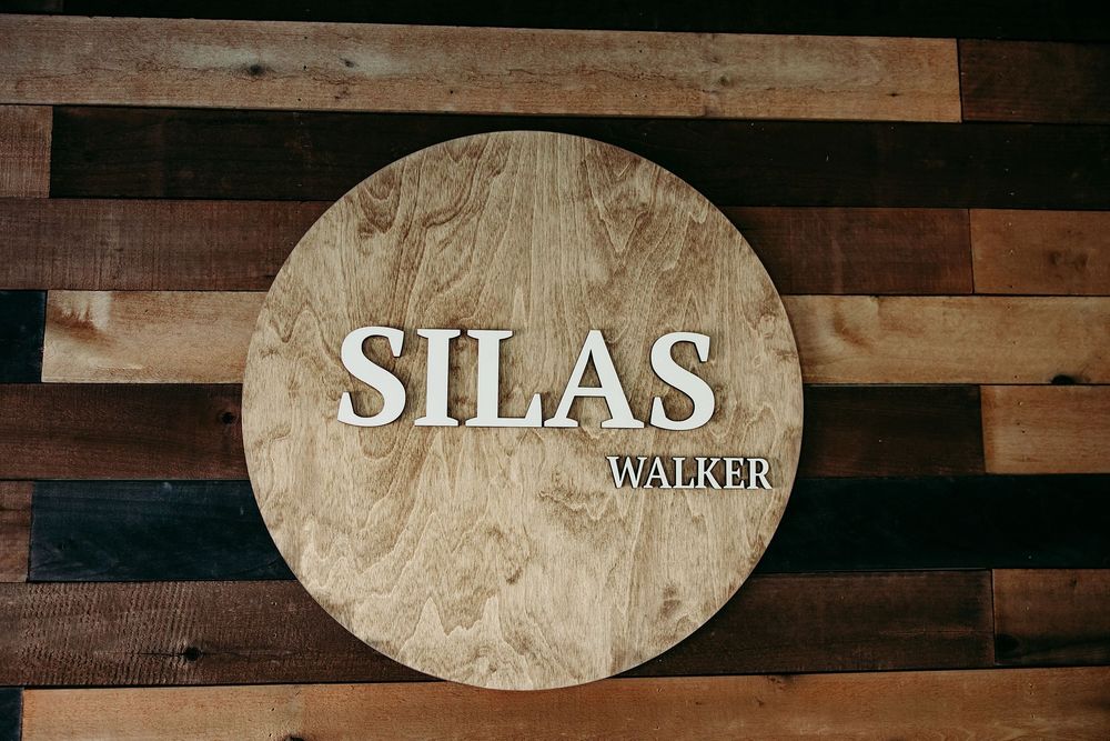 Rustic wooden wall art displays oval-shaped name plaques with text against a weathered plank background.