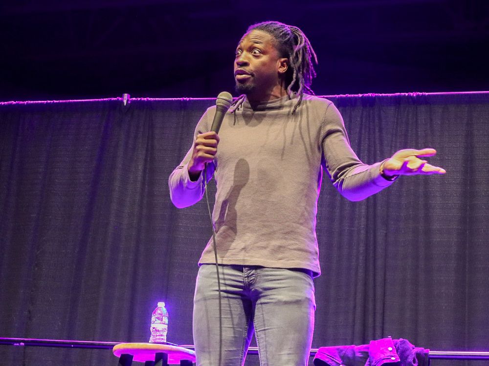 A performer speaks on stage under purple lighting during a show.