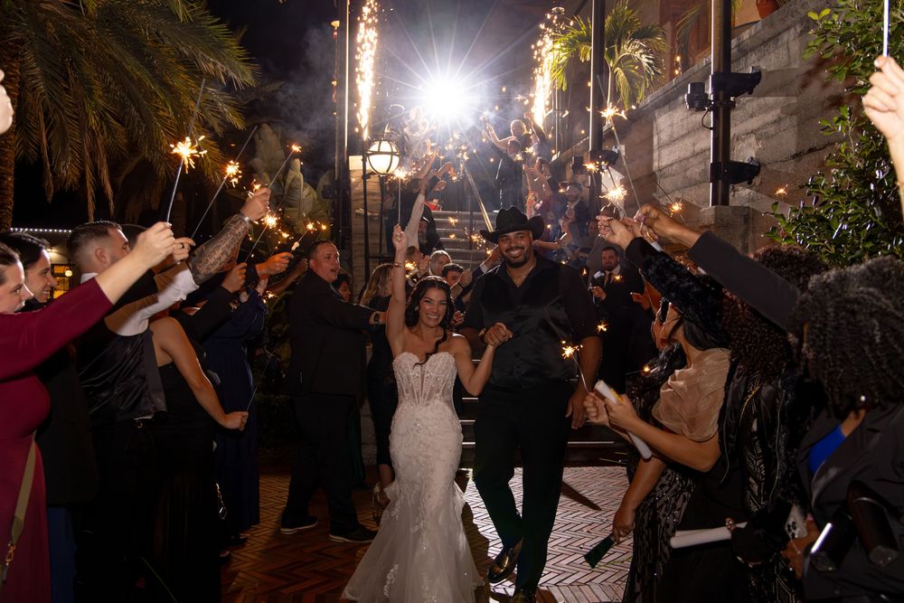 Wedding guests hold sparklers creating a magical illuminated pathway at an outdoor evening celebration.