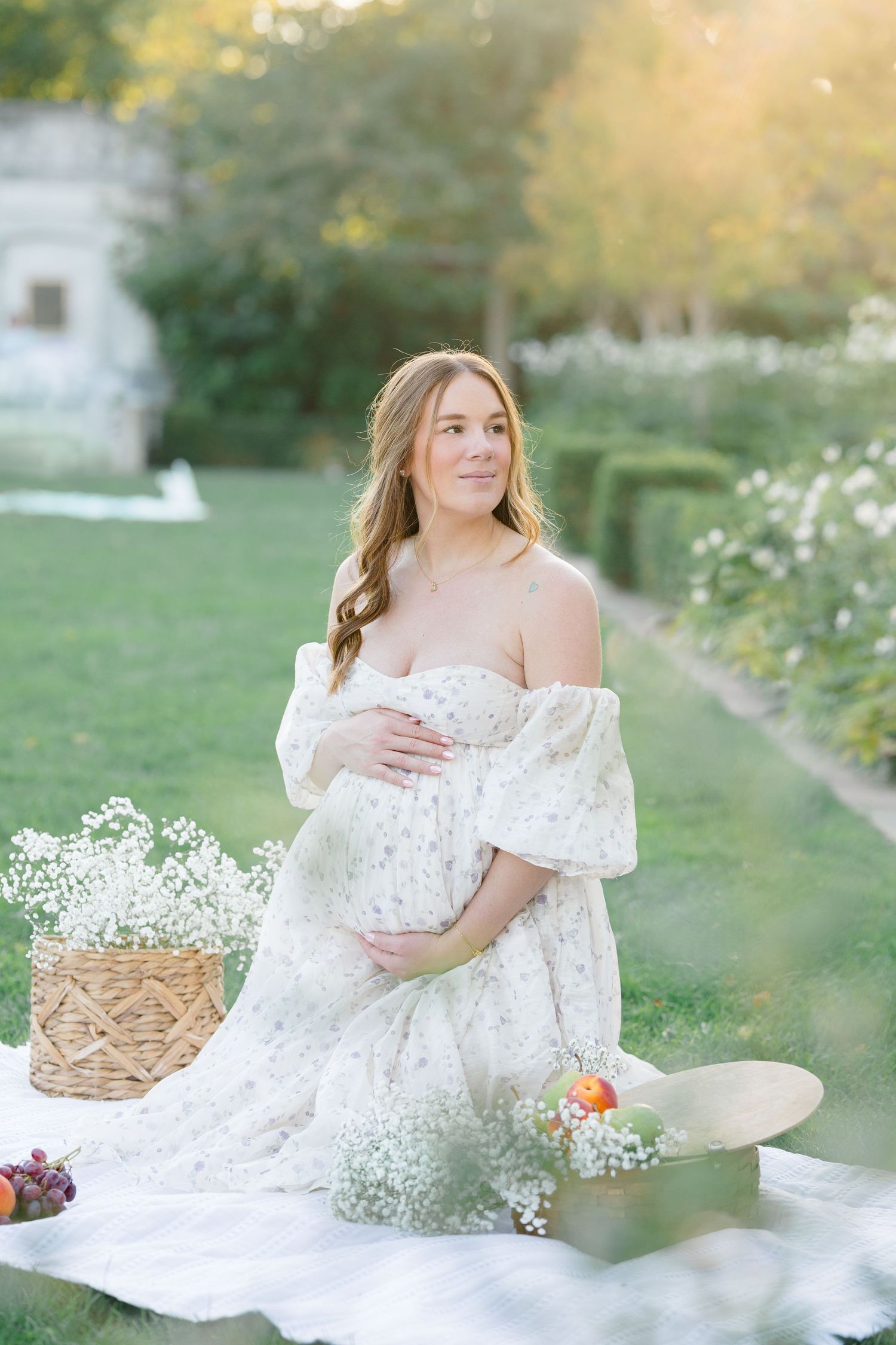 An expecting mom on picnic blanket surrounded by glowing sunlight, fruit, and delicate floral during a maternity session in Pittsburgh.