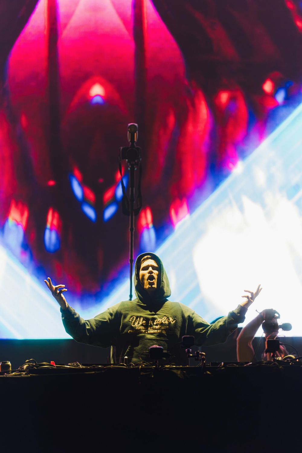 DJ performs on stage with dramatic red and blue lighting effects during an electronic music concert.