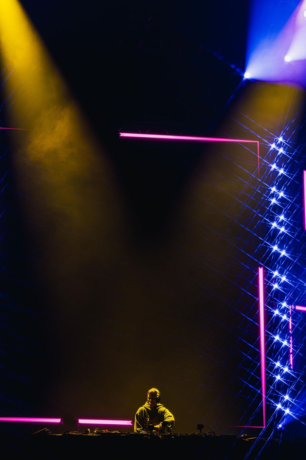 DJ performs on stage with dramatic blue and pink lighting effects creating an atmospheric nightclub environment.