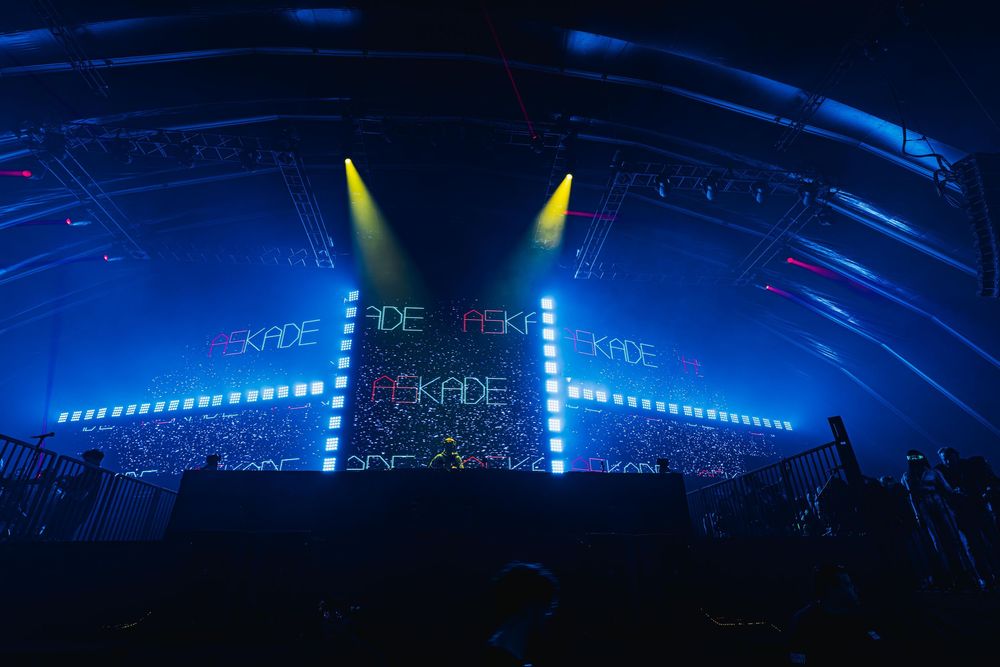 Concert stage illuminated with vibrant blue lighting and dramatic spotlights creating an atmospheric performance environment.