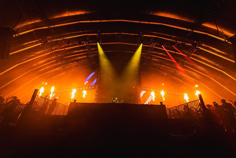 Concert crowd silhouettes against dramatic orange lighting and stage effects during a live music performance.
