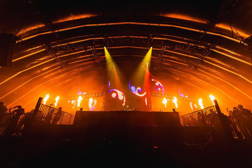 Concert stage illuminated with dramatic orange lighting and fire effects creating an intense atmosphere during performance.