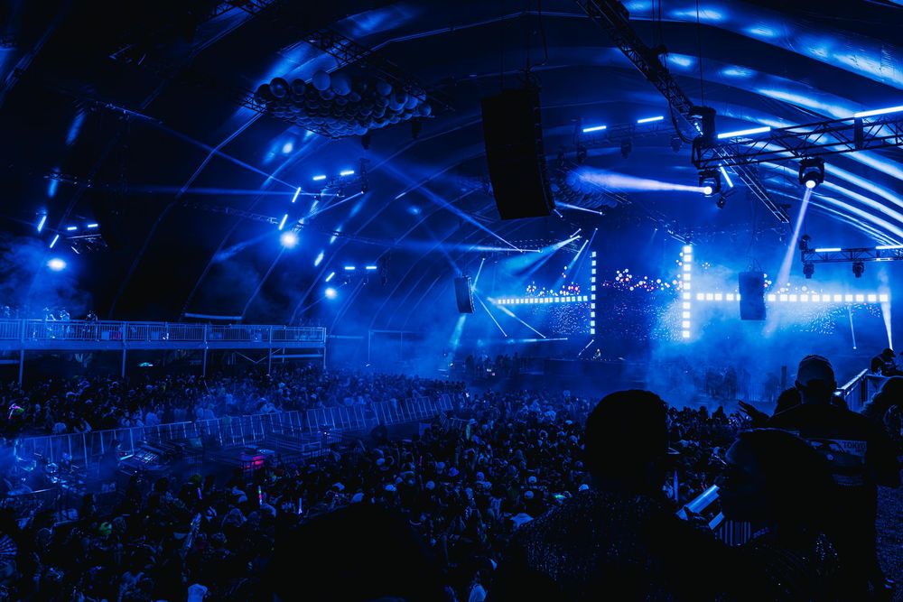 Concert venue illuminated in vibrant blue lights with a large crowd enjoying a live performance on stage.