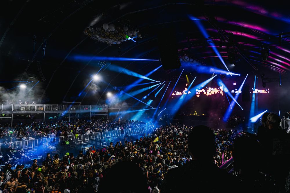 Concert venue filled with crowd under dramatic blue lighting and laser beams during nighttime performance.