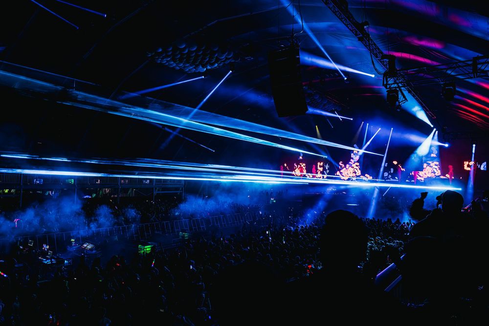 Concert stage illuminated with vibrant blue laser lights creating dynamic patterns during a live performance.