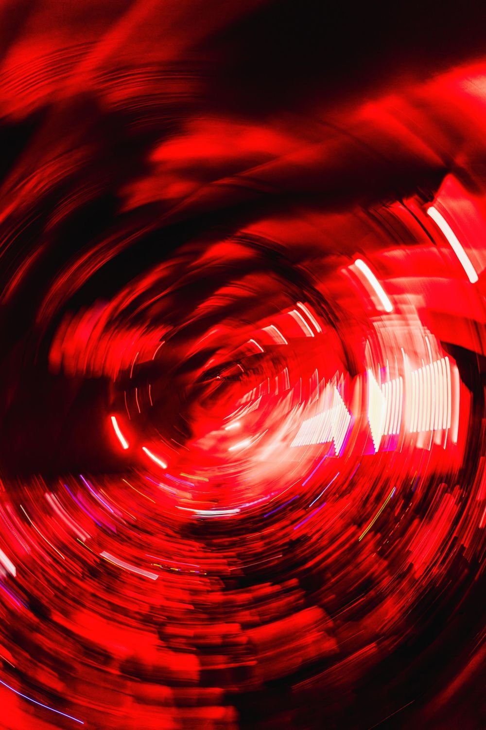 Abstract red spiral pattern with motion blur creates a dynamic swirling vortex effect against dark background.
