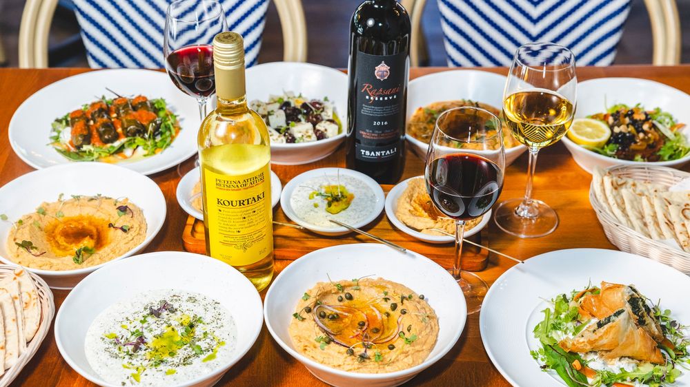 An overhead view of a long dining table filled with various plates of food, wine glasses, and drinks.