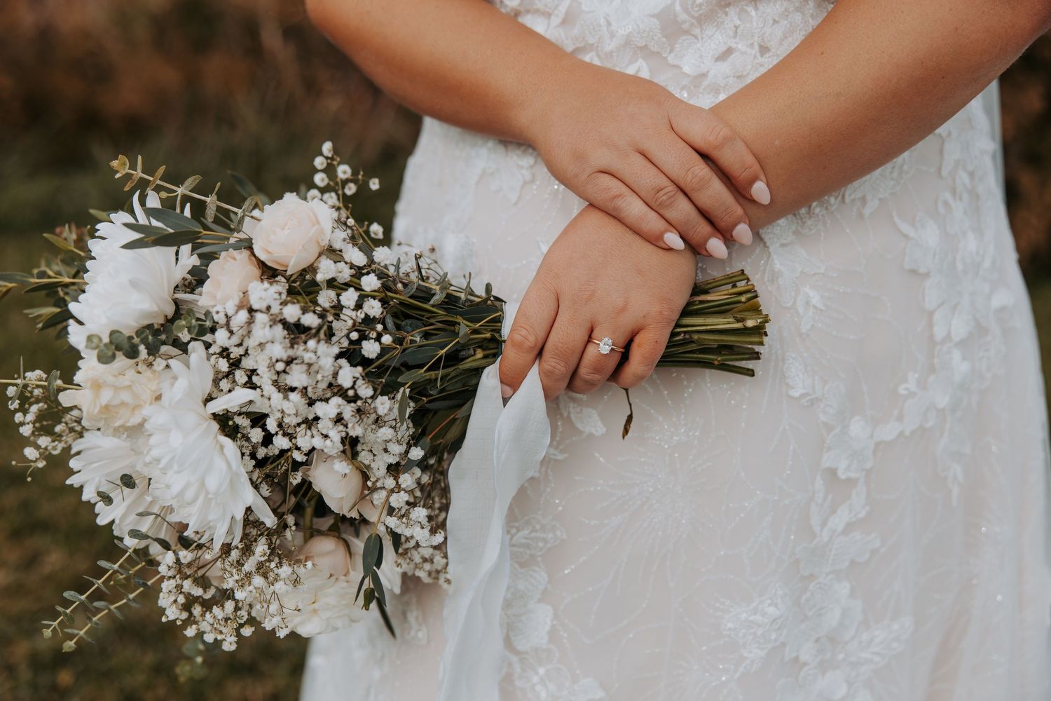 A bride in a flowing white wedding dress sits gracefully under weeping willow trees during a fall photoshoot.