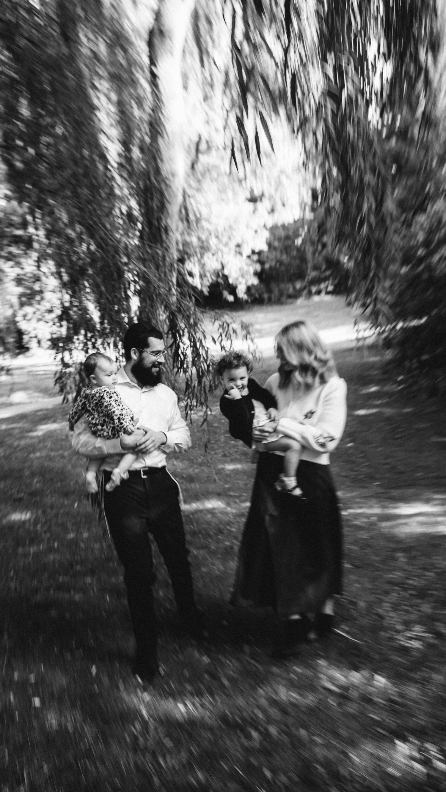 A black and white vintage photograph shows a family group standing together under trees on a sunny day.