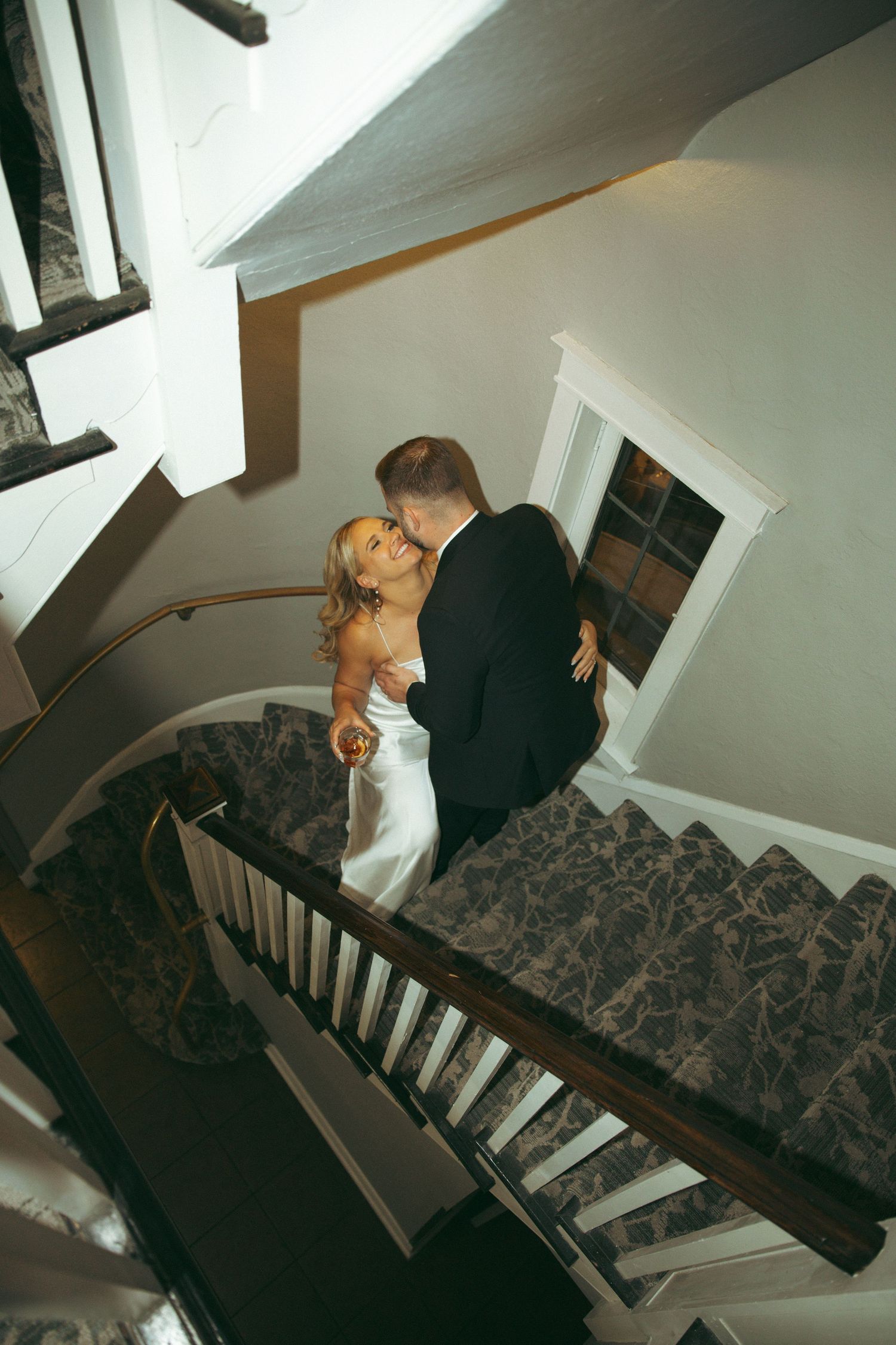 A couple in formal wedding attire embraces while standing on a staircase during a romantic photo shoot.