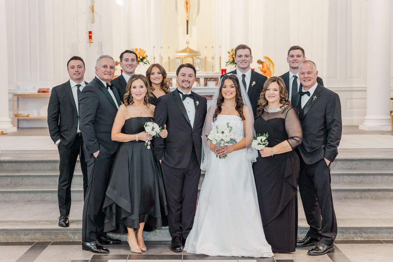 Wedding party poses together on elegant white stone steps in formal attire for group photos.